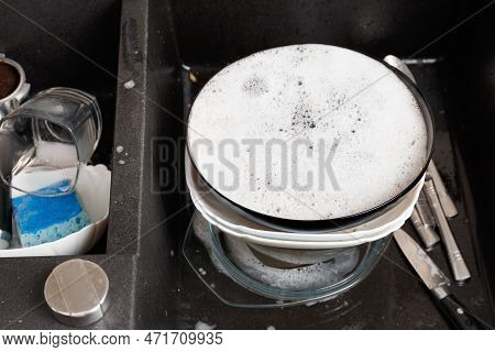Washing Dishes Concept. Dirty Dishes With Foam From Detergent In A Black Stone Sink In The Kitchen T