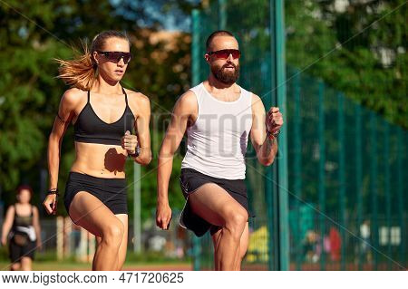 Althetes Man And Woman 25-35 Years Old, Posing For The Camera, Smiling, Running Against The Backdrop