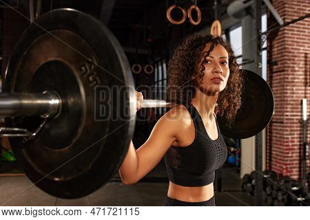 Young Pretty African American Sports Woman In Fitness Gym Lifting Up Empty Bar In Gym, Doing Warm Up