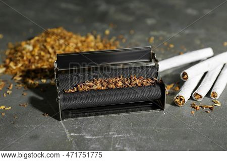 Roller With Tobacco And Hand Rolled Cigarettes On Dark Grey Table