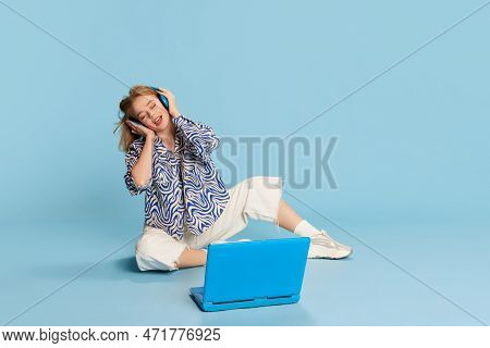 Beautiful Happy Young Girl Listening To Music In Headphones On Laptop And Singing Over Blue Studio B