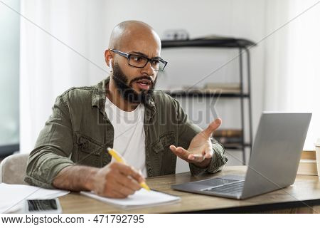 Angry Emotional Businessman Having Video Call With Employees And Taking Notes, Gesturing And Talking