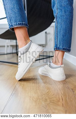 Close-up Of Female Legs In Jeans And Casual White Sneakers. Women's Comfortable Casual Shoes. White