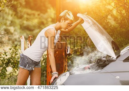 Young Sad Woman Standing Near The Road By The Broken Car In The Middle Of Nowhere. Smoke Coming Out