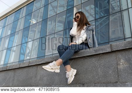 Attractive Young Girl In Sunglesses In Youth Clothing On The Summer Street. Stylish Young Woman Rest