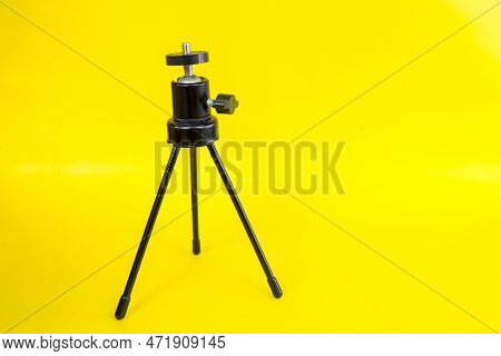 Black Mini Tripod With Steel Case And Ballhead Isolated On Yellow Background.
