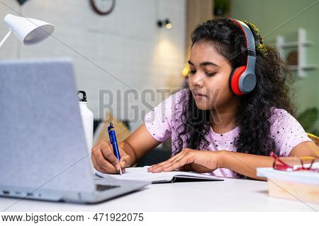 Girl Student Making Notes From Online Class Using Laptop At Home By Wearing Wirless Headphones - Con