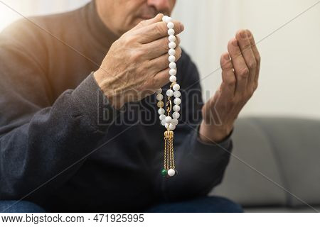 An Elderly Man Prays With A Rosary And The Flag Of The United Arab Emirates