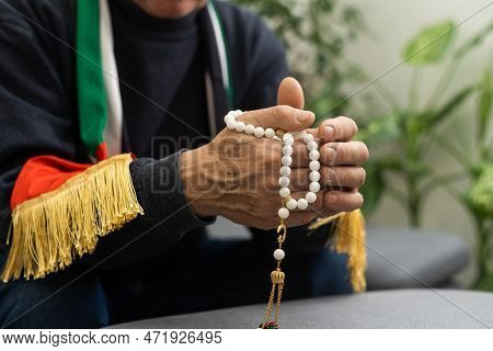An Elderly Man Prays With A Rosary And The Flag Of The United Arab Emirates