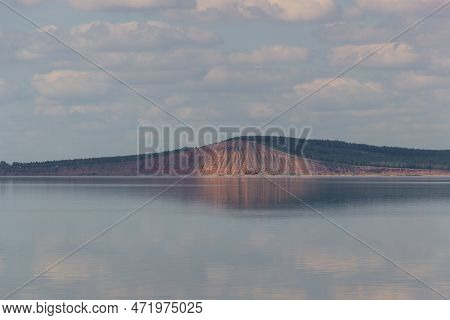 Lake With Clouds In The Sky, Red Hill With Forests On Background. Hill Symmetric Reflection In The W