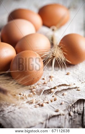  fresh brown eggs, wheat seeds and ears on linen background 