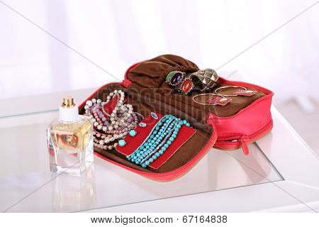 Handbag with accessorises and perfumes in bottles on table on  home interior background