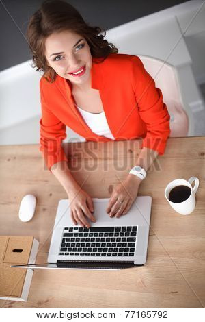 Attractive woman sitting at desk in office, working with laptop