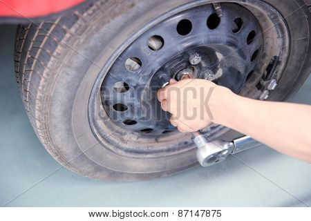 car mechanic screwing or unscrewing car wheel of lifted automobile by pneumatic wrench at repair ser