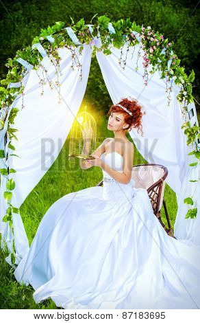 Beautiful bride with chaming red hair sitting under the wedding arch. Wedding dress and accessories. Wedding decoration. 