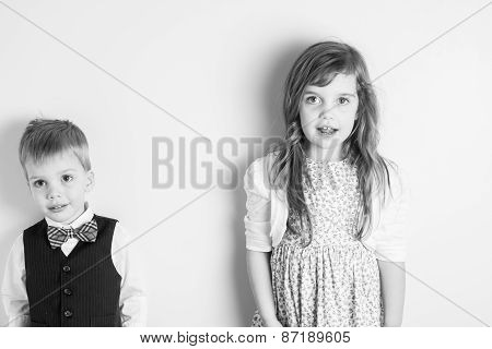Black And White Portrait Of Brother And Sister Standing Against A Wall