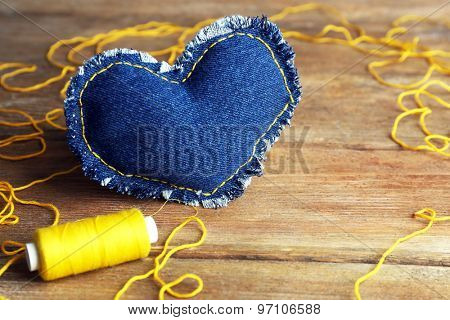Denim heart and thread on wooden background