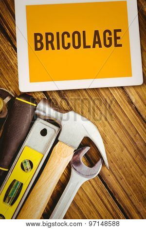 The word bricolage and tablet pc against desk with tools