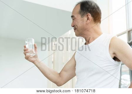 Asian senior man holding glass of water at a gym. Tired thirstily. freshness.