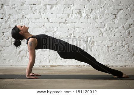 Young yogi attractive woman practicing yoga concept, stretching in Purvottanasana exercise, Upward Plank pose, working out, wearing sportswear, black tank top, pants, full length, loft background