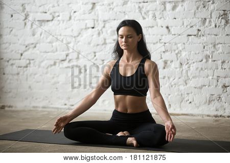 Middle aged yogi attractive woman practicing yoga concept, sitting in Half Lotus exercise, Siddhasana pose, working out, wearing black sportswear bra and pants, full length, white loft background