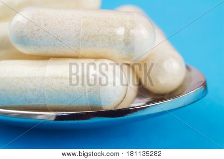 White capsules of glucosamine chondroitin healthy supplement pills in the spoon on blue background macro image