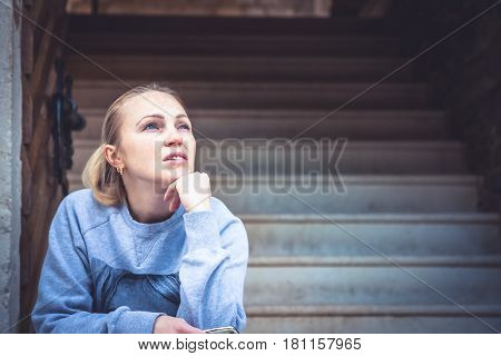 Thinking young woman sitting on stairs and look up with copy space. Concept for forecasting and way forward