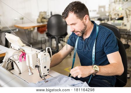 Good looking young man working as a tailor and using a sewing machine in a textile factory