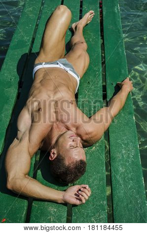Attractive young, athletic muscle man laying down on a wood pier, looking at camera