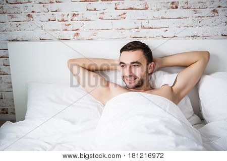 Handsome Well Built Man Resting In His Bed In Morning With Smile On Brick Wall In Room At Home