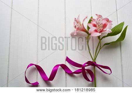 Flat lay. Beautiful flowers with bow and ribbon on the white wooden table