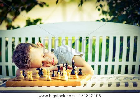 Tired boy fell asleep at the chessboard. child tired of playing chess