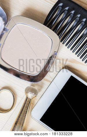 Light beige powder for the face, white mobile phone, comb, gold scissors and mascara in a golden tube on a light wooden table. Women's tricks concept