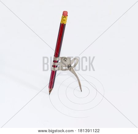 Simple school metal compass and the inserted into it common pencil with attached eraser drawing the concentric circles on a white sheet of a paper