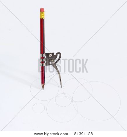 Simple school metal compass and the inserted into it common pencil with attached eraser drawing the circles of different diameters on a white sheet of a paper
