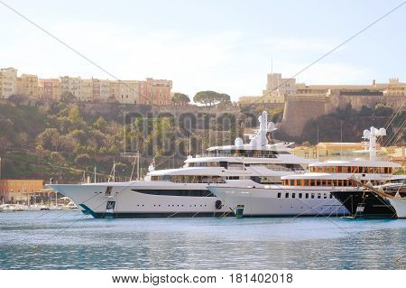 Luxury boats moored in marina in south of France with Grimaldi Royal Palace on hill in background