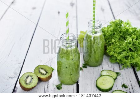 green smoothie, healthy, organic drinks with fresh vegetables and fruits. Two smoothie glasses with drinking straw on a white table. Close-up shot.