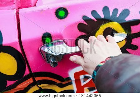 Female hand holding silver doorhandle of bright colorful car at festival