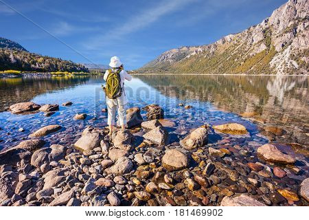 The elderly woman with green tourist backpack taking pictures of a lake in Bariloche. The concept of exotic and extreme tourism. Picturesque summer in Argentina