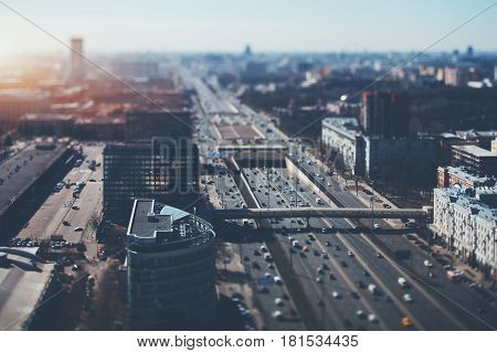True tilt shift shooting of highway in metropolis from high point: multiple residential and office buildings parking many cars on busy streets of the city crosstown traffic sunny springtime