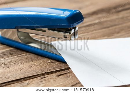 blue stapler and paper sheet on wooden background, close-up