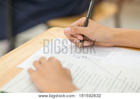 students hand holding pencil fill in Exam carbon paper sheet or test paper multichoice on wood desk education concept