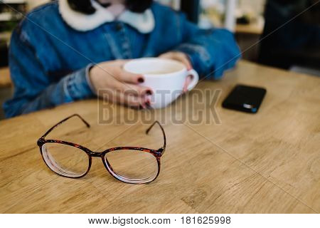 glasses on a wooden table for sight against the background of a girl with a coffee in a cafe