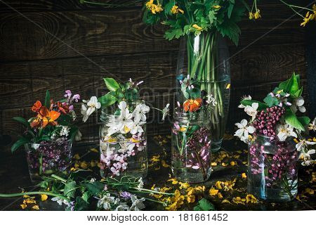 Vivid picturesque bouquets of colorful spring flowers in glass vases bottles on a dark wooden background table