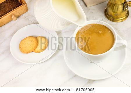 Milk just poured into a cup of coffee, with vintage coffee grinder and pot in the background. Selective focus and a place for text