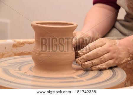 hands of a potter, creating an earthen jar on a pottery wheel