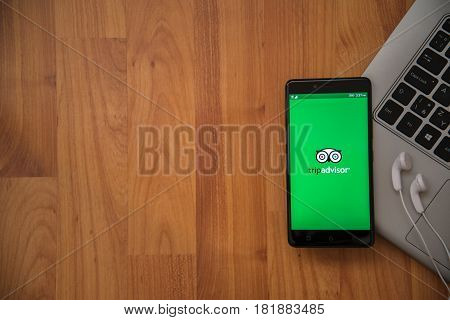 Los Angeles, USA, april 16, 2017: Tripadvisor application on smartphone with earphones and notebook on wooden background.