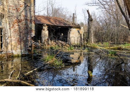 Old brick abandoned house with a ruined wall swamped by a swamp