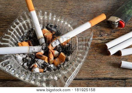 A close up image of a glass ashtray with lit cigarettes and cigarette ashes.