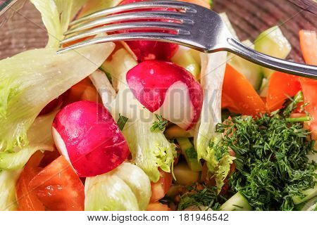 Fresh vegetables salad in a glass bowl. Mix from the cut radish pomidory and cucumbers. Close up selective focus